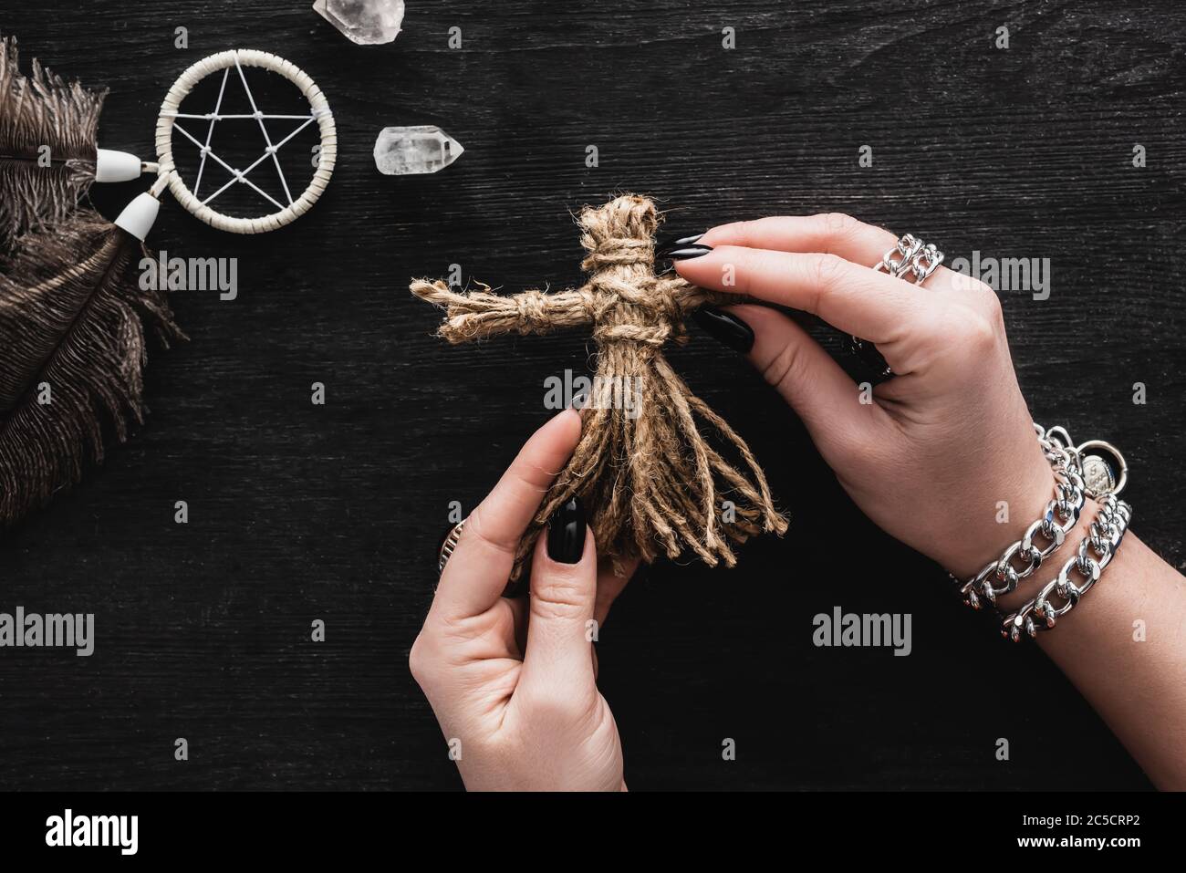 Draufsicht auf Frau, die Voodoo Puppe in Händen neben Pentagramm und Kristallen auf Schwarz hält Stockfoto