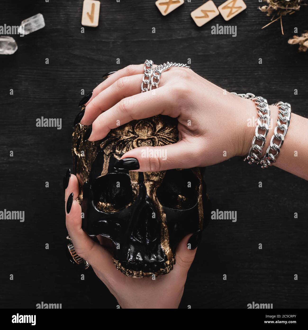 Nahaufnahme einer Frau, die den Schädel in der Nähe von Runen und Kristallen auf Schwarz hält Stockfoto