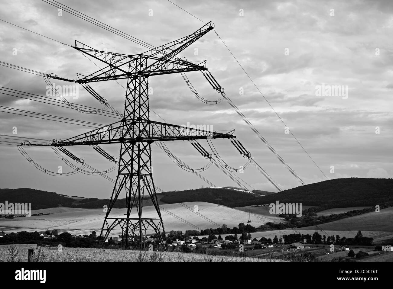 LUCKA bei GIRALTOVCE, SLOWAKEI, JULI 27 2019: Massive Stahlhochspannungs-Pole im goldenen Getreidefeld über einem kleinen Dorf mit bewölktem Himmel. Stockfoto