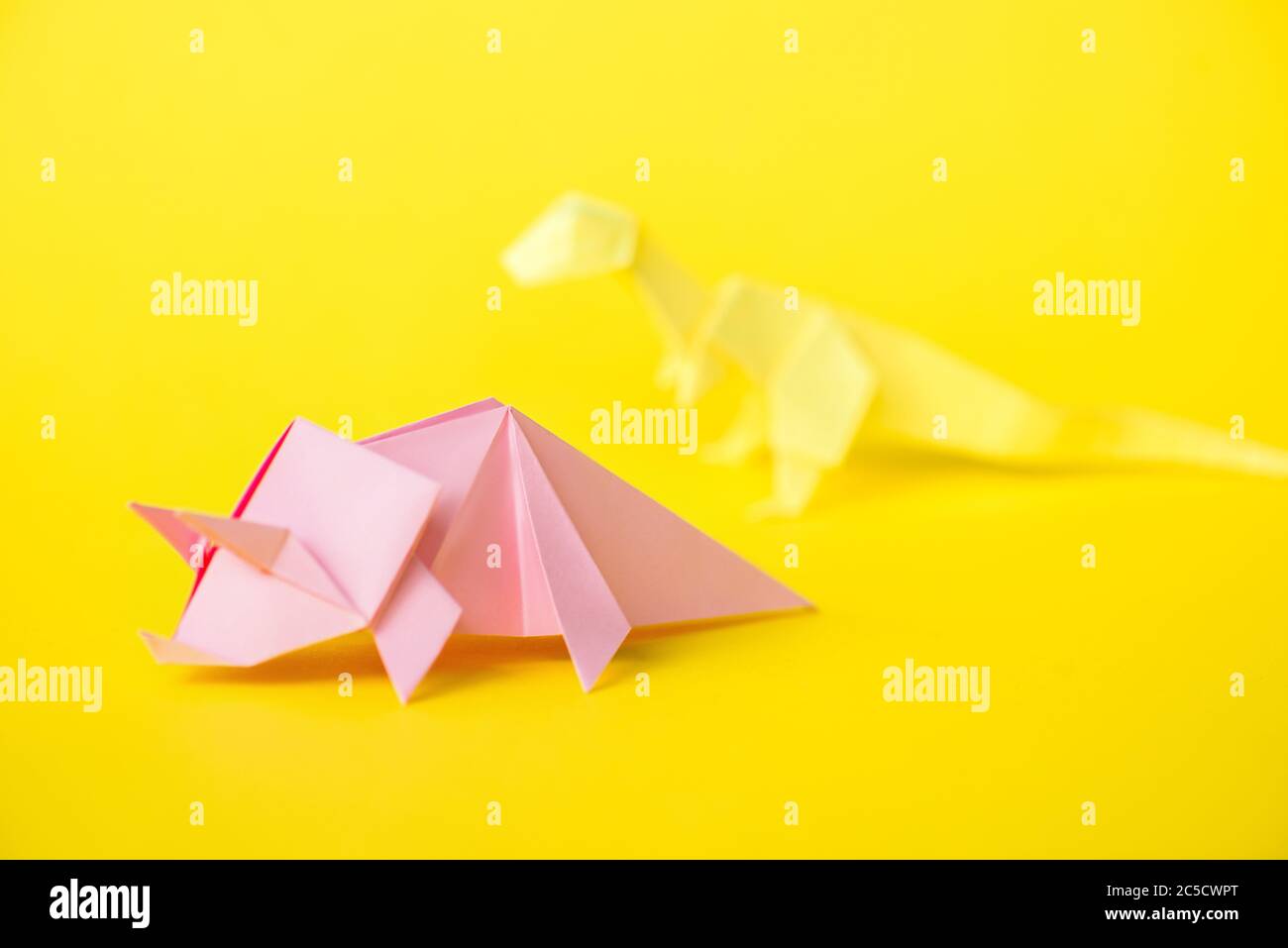 Selektiver Fokus von rosa Papier Nashorn in der Nähe Origami-Dinosaurier auf gelb Stockfoto