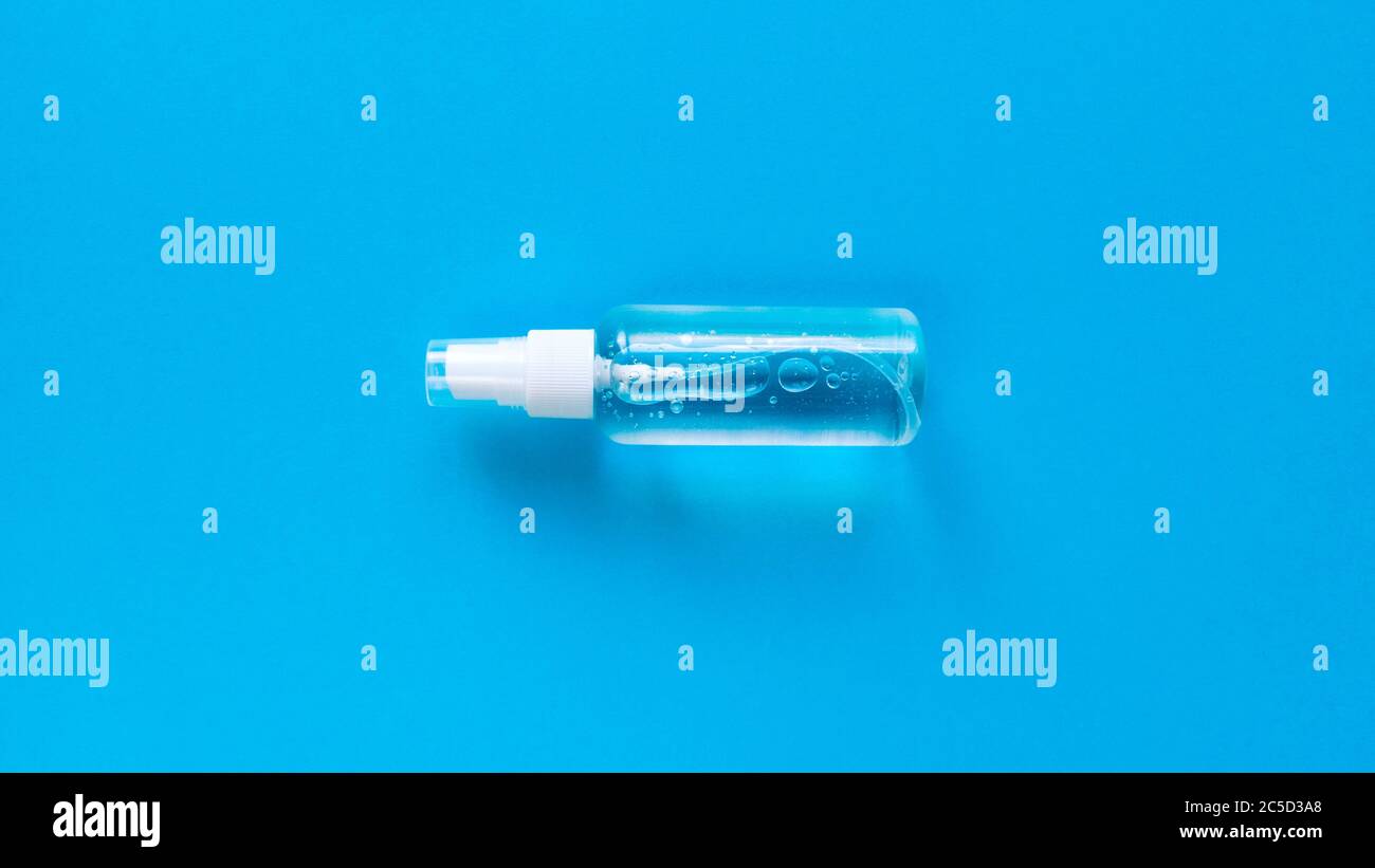 Transparente Flasche mit Sprühkappe in der Mitte des blauen Hintergrunds. Einfache flache Lay mit Pastellpapier Textur. Medizinisches Konzept. Bestand Stockfoto