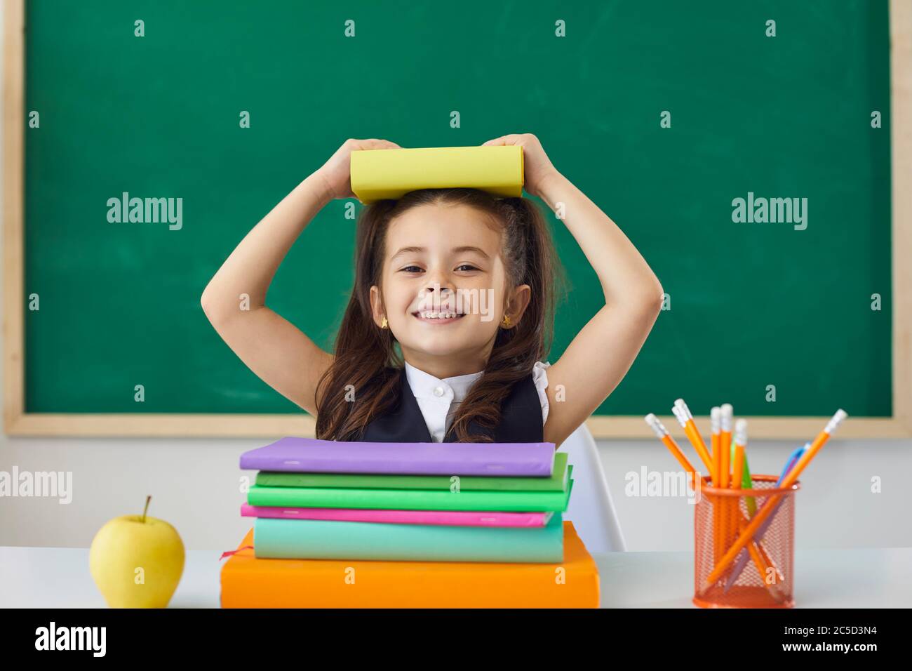 Konzept zurück in die Schule. Happy Schulmädchen hält ein Buch über ihren Kopf, während sie in einer Lektion in der Klasse sitzen. Stockfoto