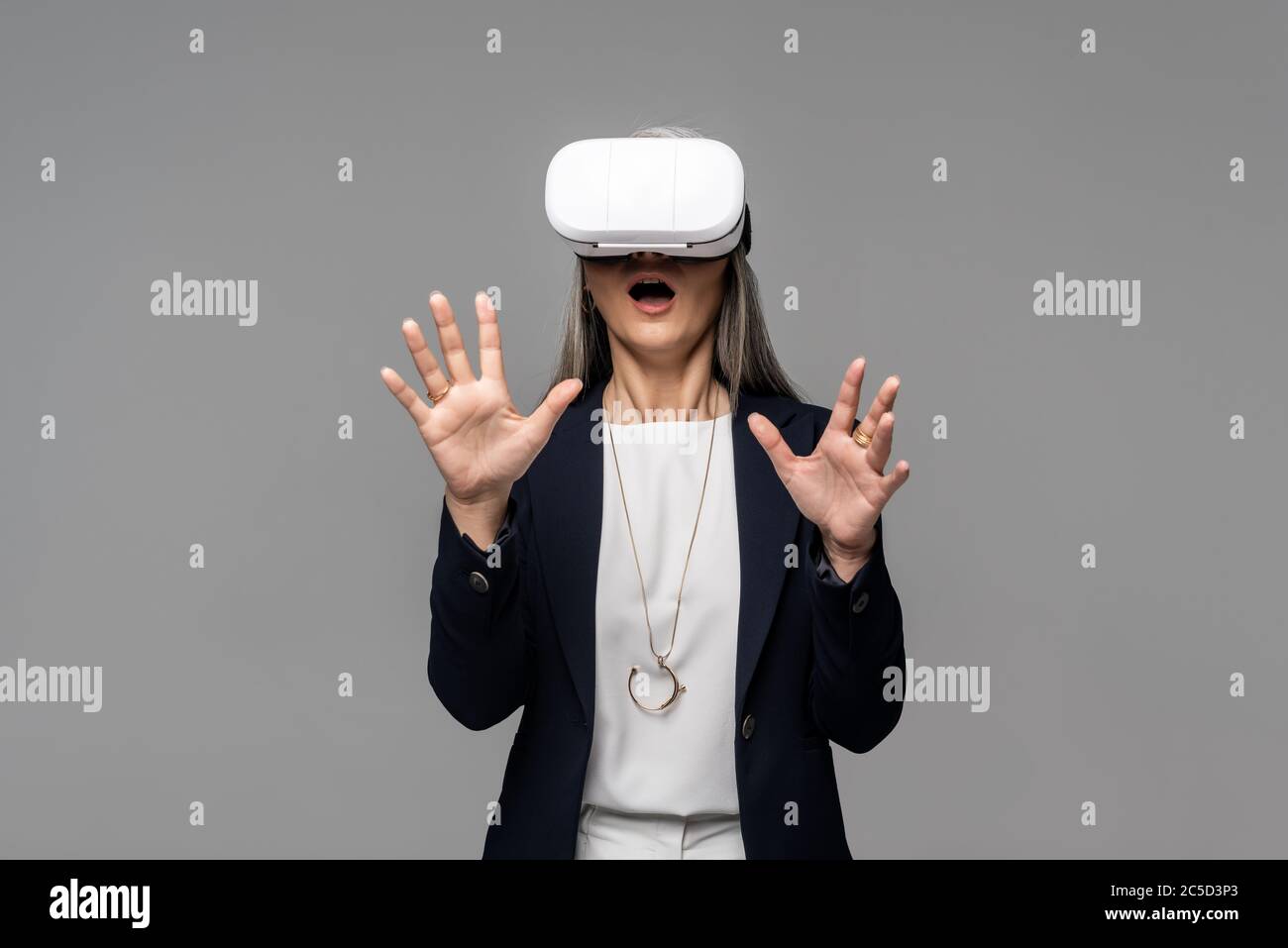 Schockiert Geschäftsfrau gestikulieren und mit Virtual-Reality-Headset isoliert auf grau Stockfoto