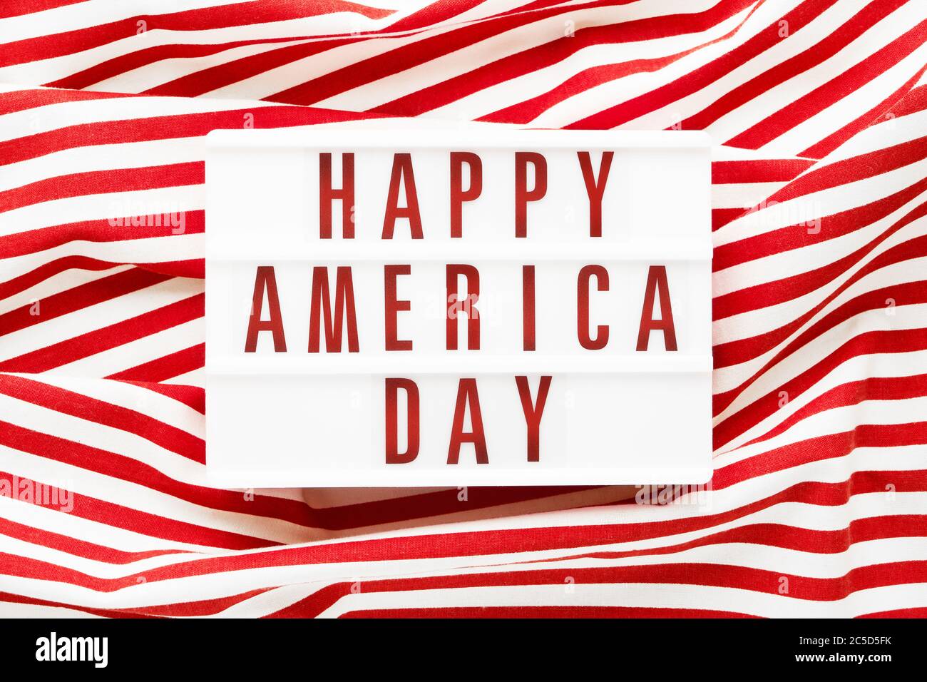 HAPPY AMERICA DAY in Leuchtkasten auf rotem Hintergrund geschrieben. Draufsicht, Kopierbereich. Konzept des Unabhängigkeitstages Stockfoto