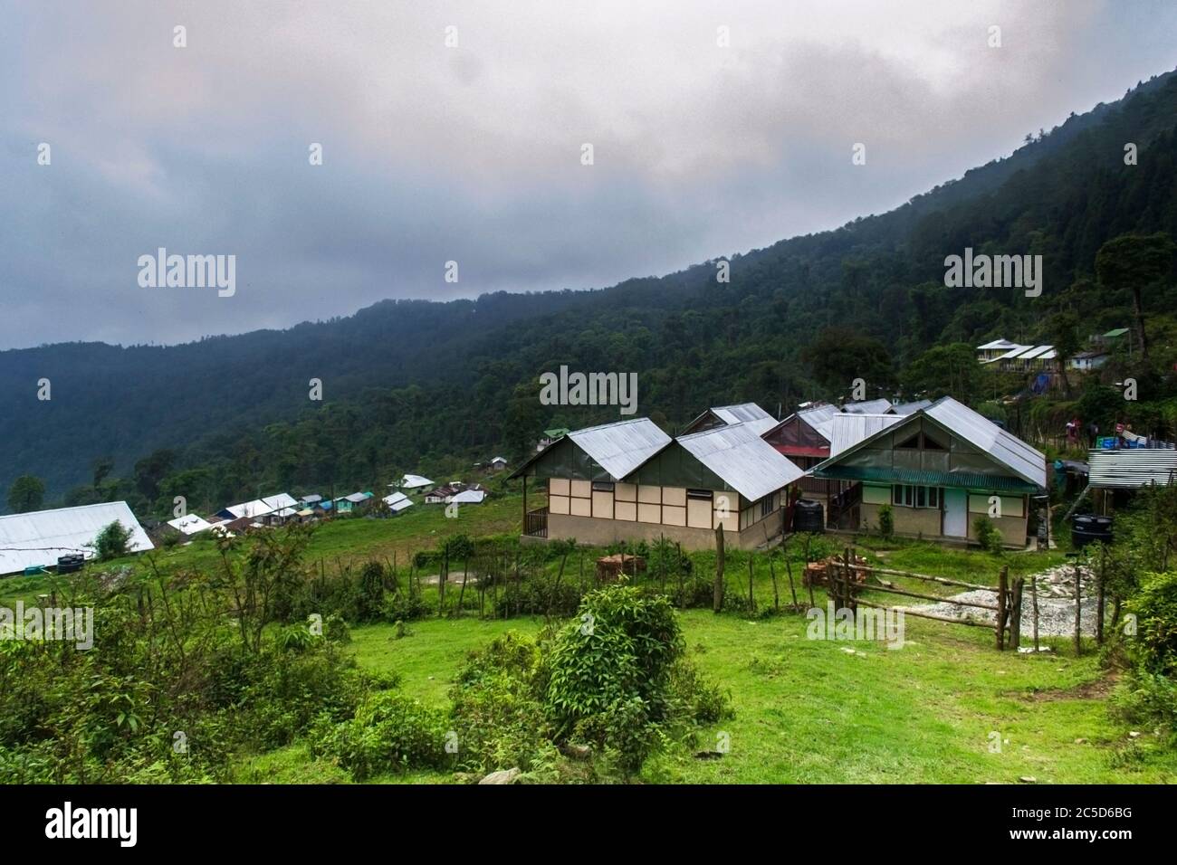 Bergtal mit vielen Wolken und grünen Pinien und kleinen Dorfhäusern Stockfoto