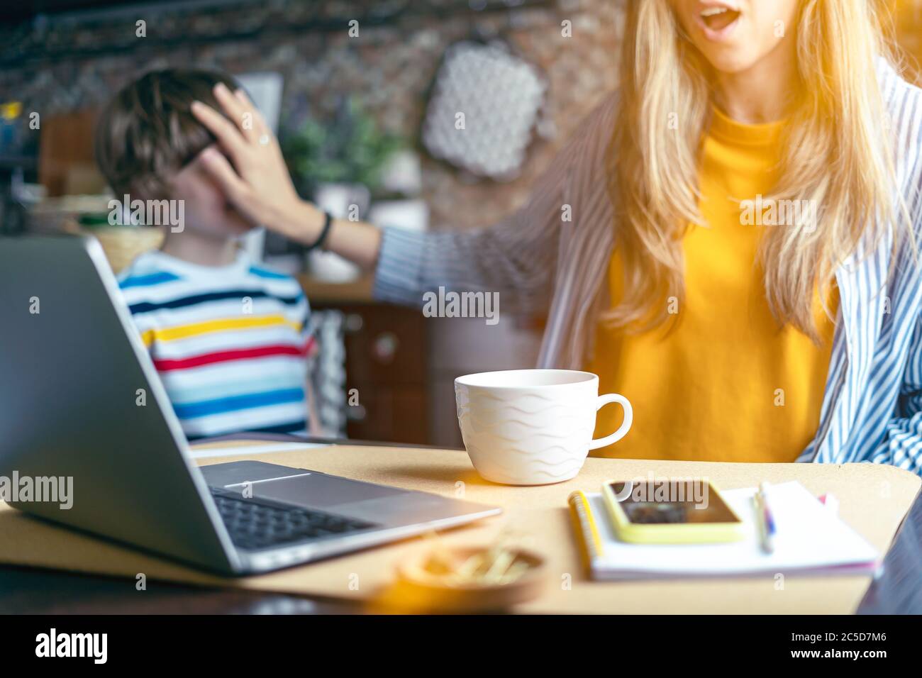 Mutter arbeitet von zu Hause und Online-Bildung mit Kind. Gestresst mit Computer und Telefon. Kind machen Lärm und stören Frau bei der Arbeit. Heimschooling und Stockfoto