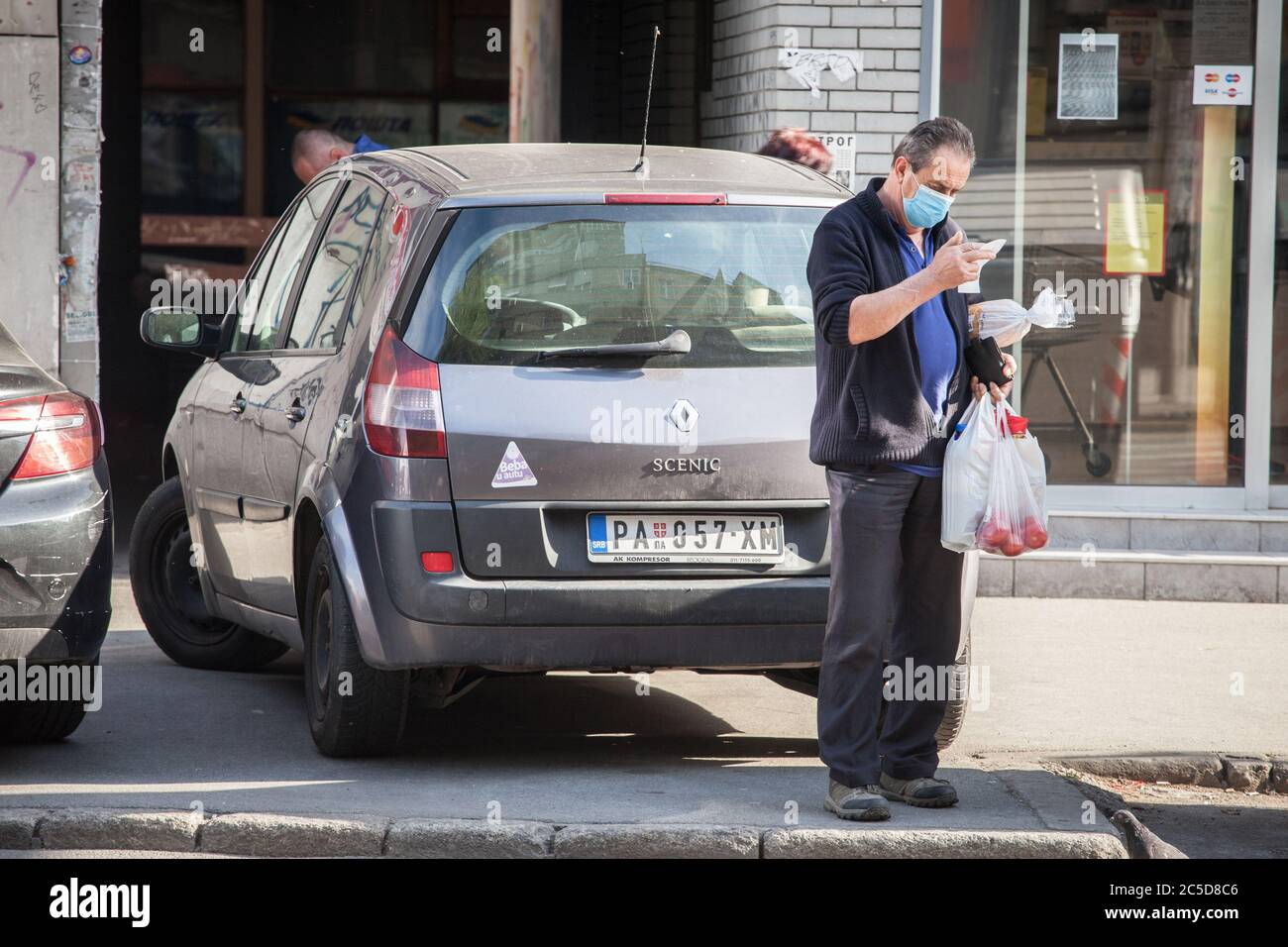 BELGRAD, SERBIEN - 9. MAI 2020: Alter älterer Mann mit einer Atemmaske, der den Preis seiner Grocieries in der Straße von Belgrad während der Überprüfung Stockfoto