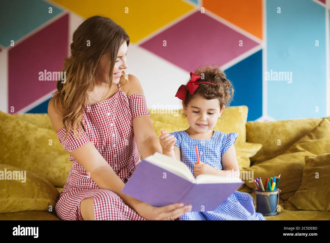 Schöne junge Mutter mit ihrer kleinen niedlichen Tochter glücklich Zeichnung in Malbuch mit Filzstiften während die Zeit zusammen auf dem Sofa zu Hause verbringen Stockfoto