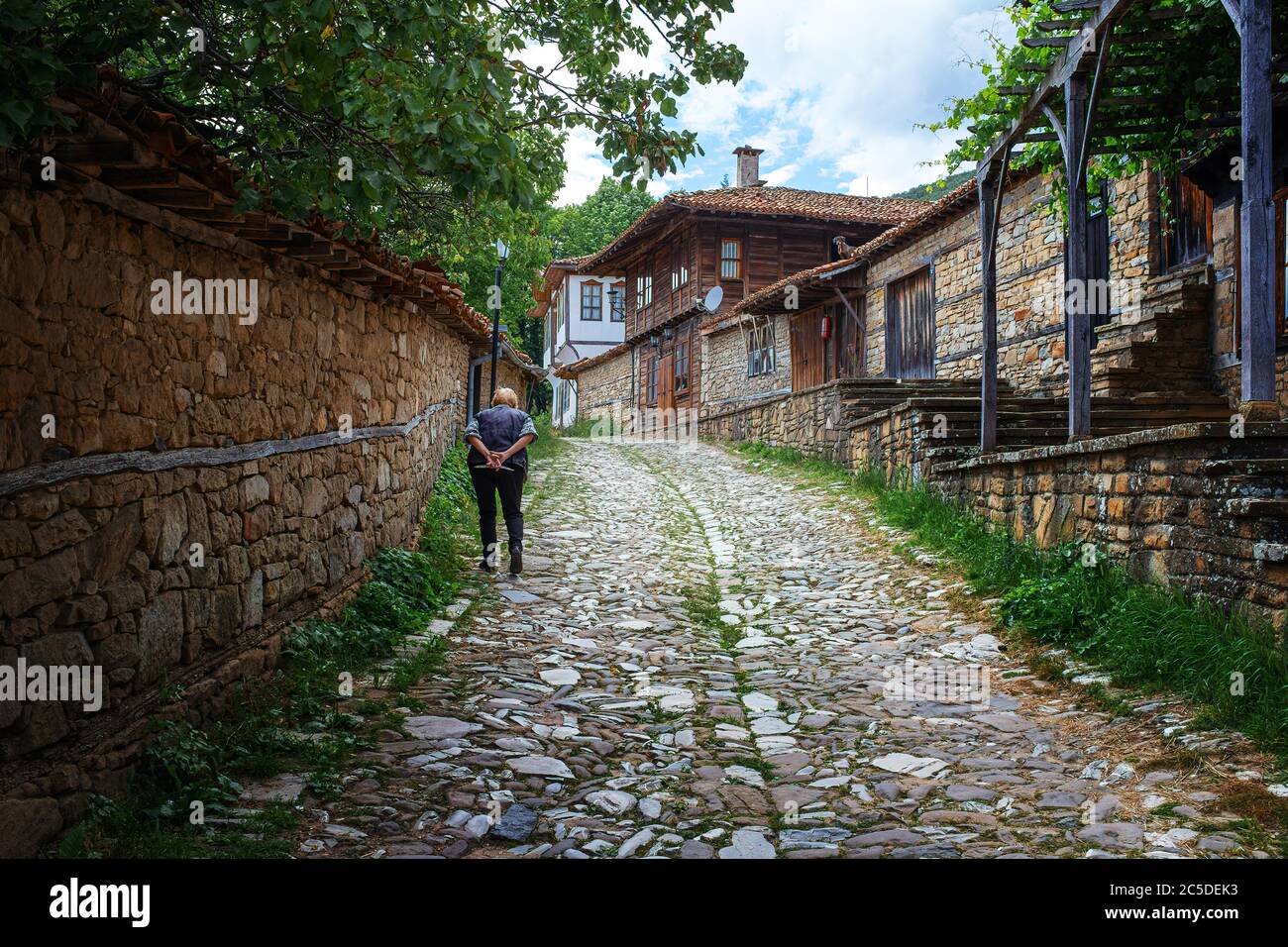 Alte bulgarische Dame mit Händen hinter Rücken zu Fuß auf gepflasterten sttreet in Zheravna Dorf Bulgarien Stockfoto