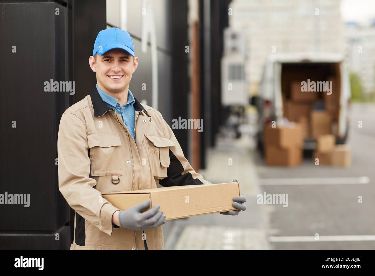 Porträt eines jungen Kuriers in uniformier Haltebox und lächelnd auf Kamera, während sie im Freien stehen Stockfoto