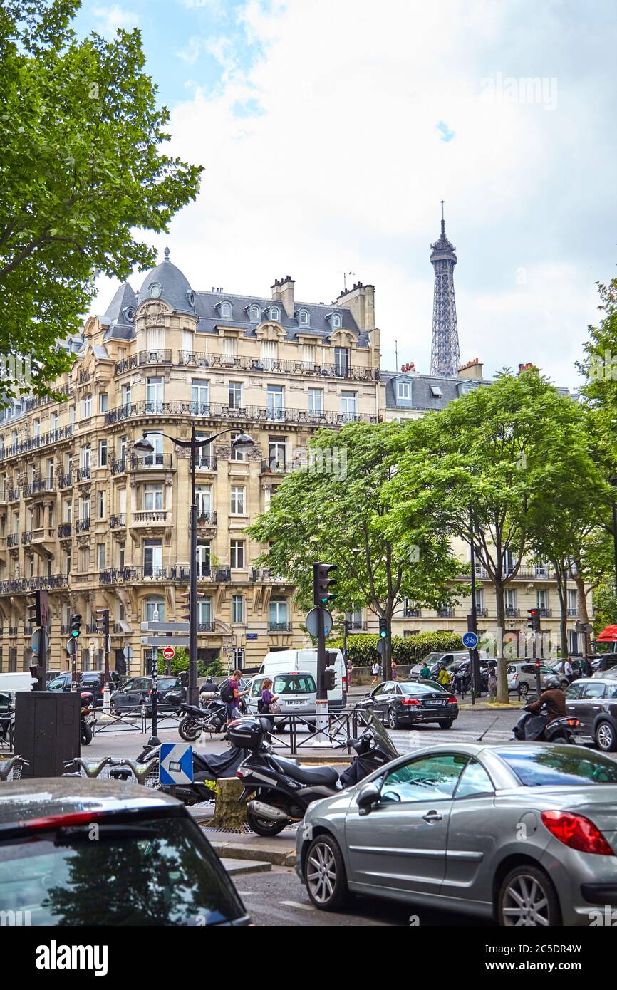 Paris, Frankreich - 19. Juni 2015: Geparkte Autos, Fahrräder, Roller auf einer schönen Stadtstraße mit grünen Bäumen. Der Turm des Eiffelturms hinter dem f Stockfoto