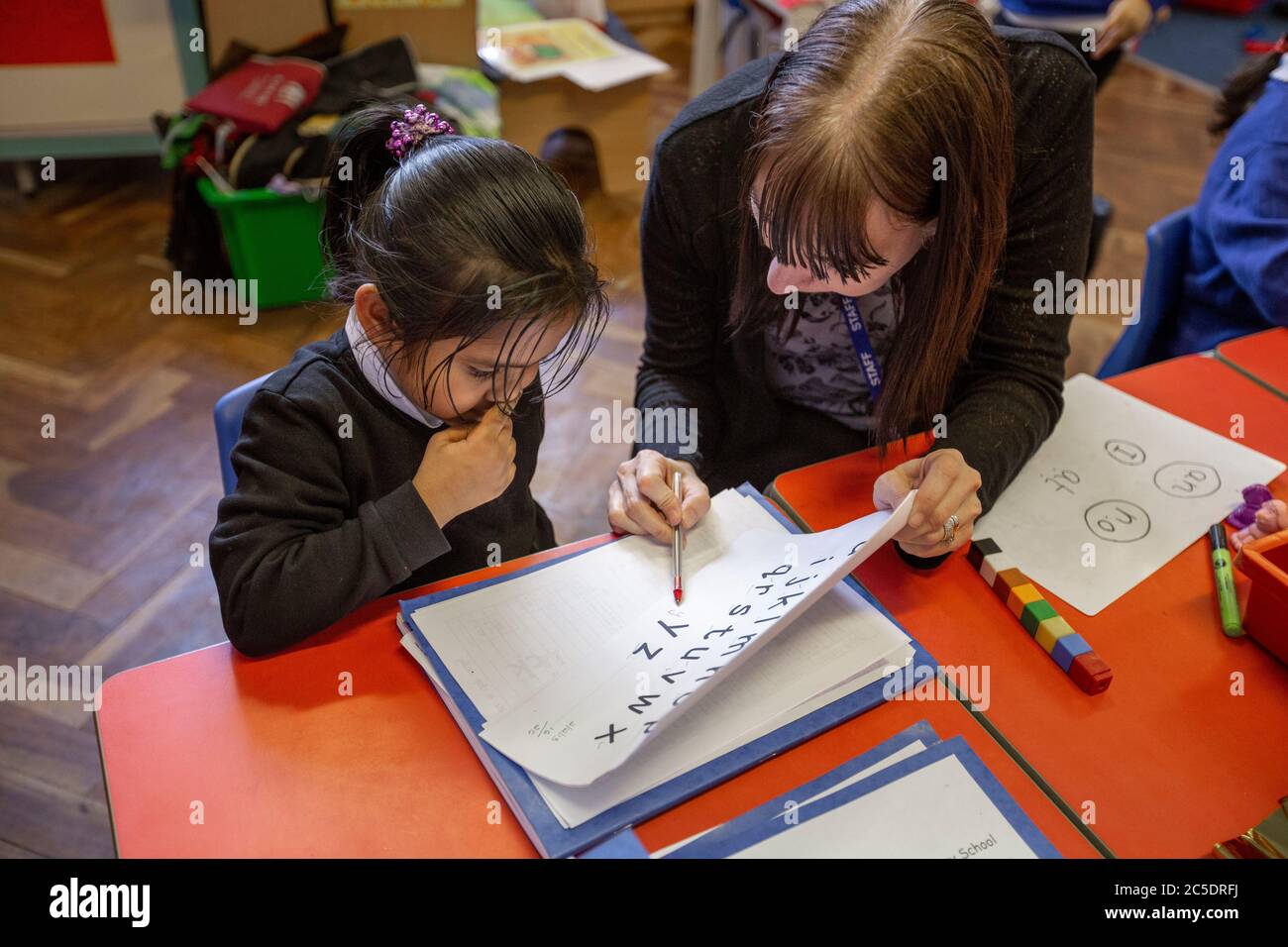 Eine Lehrerin hilft einem Schulmädchen während eines Englischunterrichts in Großbritannien Stockfoto