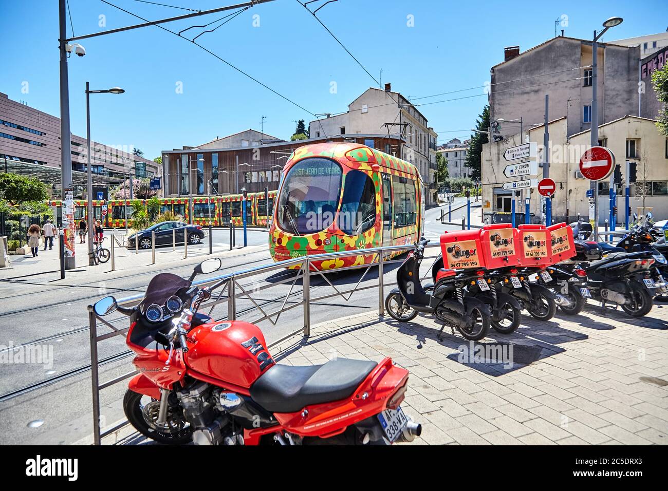 MONTPELLIER, FRANKREICH - 24. Juni 2015: Öffentliche Verkehrsmittel in der Stadt. Schöne mehrfarbige Straßenbahn. Rote Motorrad und Roller für die Lieferung von Fast Food in der Stockfoto