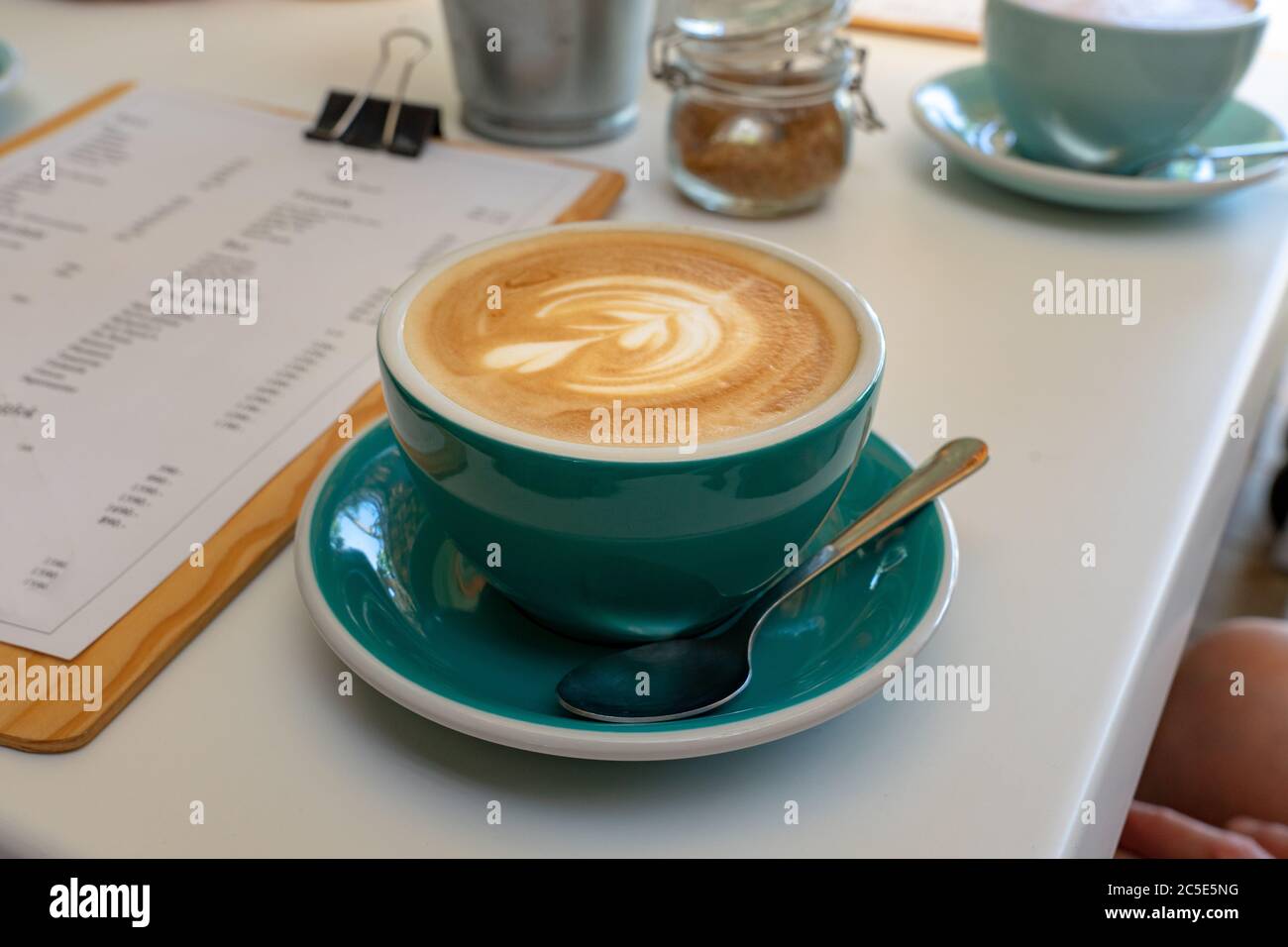 Caffee Latte Macchiato Cappuccino in blau türkis Tasse im Café-Haus mit Milchschaum Kunst. Stockfoto