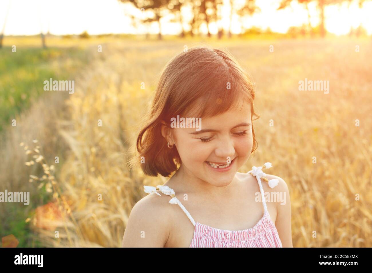 Lustiges Mädchen lacht bei einem Spaziergang über das Feld bei Sonnenuntergang. Das Konzept der echten Kindheit, digitale Entgiftung, Sommerferien, Glück. Stockfoto