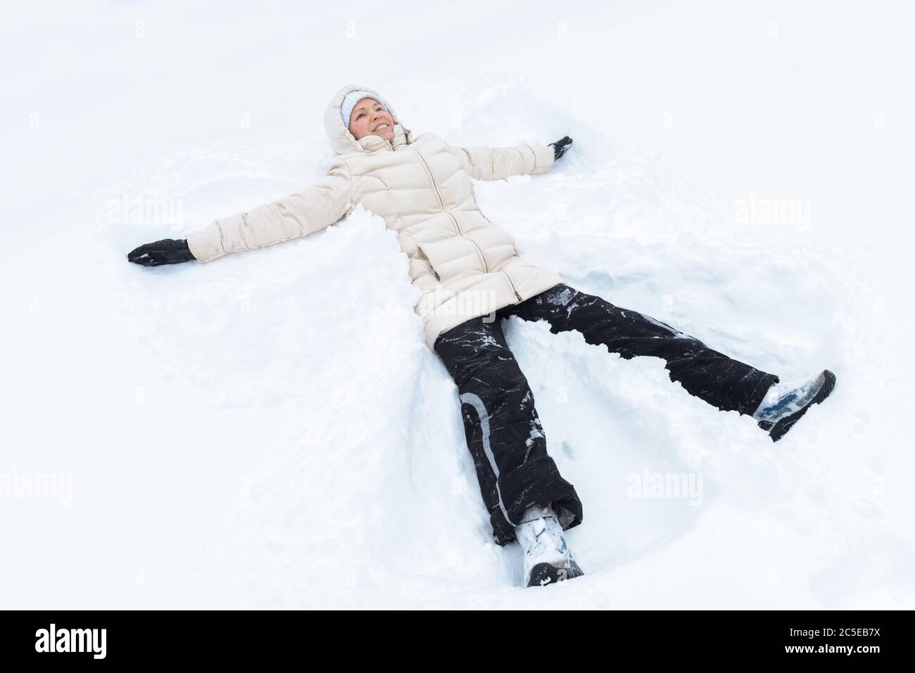 Porträt einer jungen Frau, die auf einem Schnee liegt. Das verspielte Mädchen schafft einen Schneeengel bei Schneefall. Winterspiele im Freien. Stockfoto