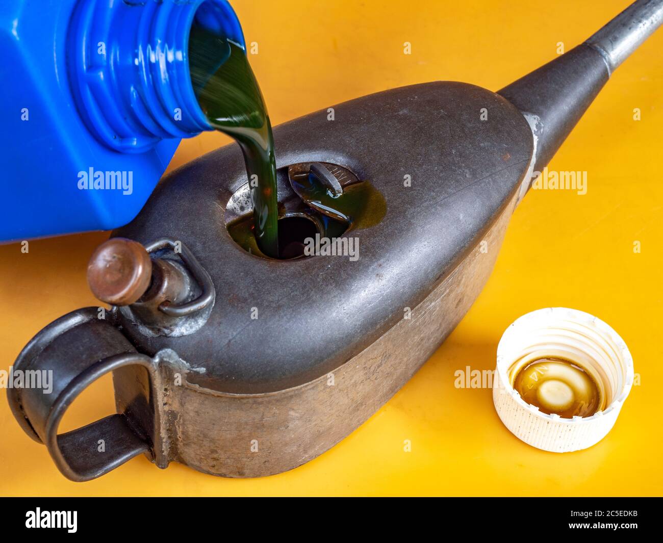 Nahaufnahme POV-Aufnahme von Öl, das aus einer blauen Plastikflasche in die Oberseite einer kleinen Weinlese-Öldose mit einem dünnen Auslauf fließt, um Öl bei einem Erhaltungsloch zu verteilen. Stockfoto