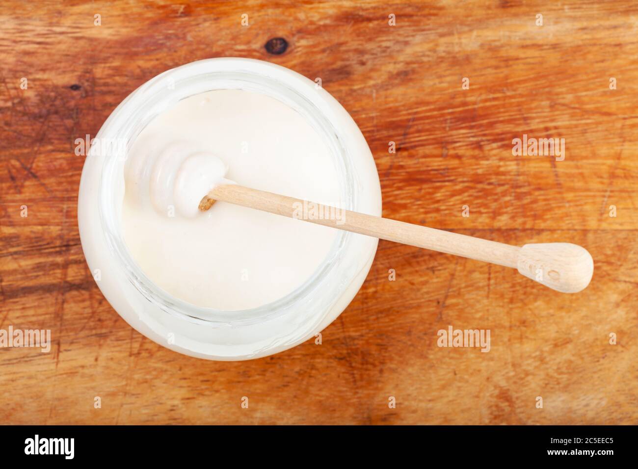 Draufsicht auf Honiglöffel im Glas mit natürlichem Bio-weißem Honig auf Holzbrett Stockfoto