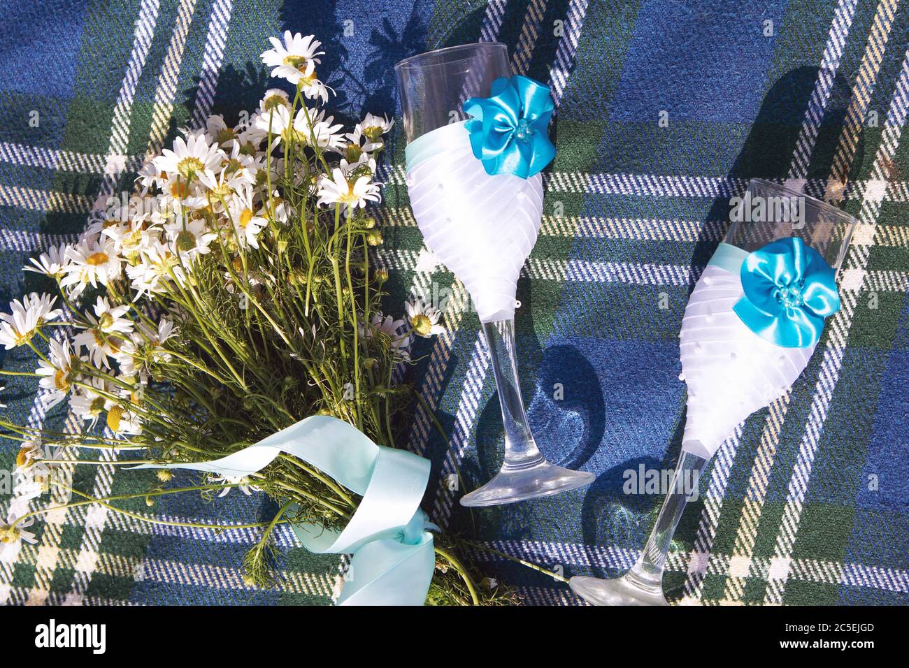 Ein Blumenstrauß aus Gänseblümchen und Hochzeitsgläsern auf einem blauem Tweed-Bettüberwurf oder -Hemd. Sommer Blumen romantischen Hintergrund. Leerzeichen für Text. Die Idee eines Romantiks Stockfoto Ein Blumenstrauß aus Gänseblümchen und Hochzeitsgläsern auf einem blauem Tweed-Bettüberwurf oder -Hemd. Sommer Blumen romantischen Hintergrund. Leerzeichen für Text. Die Idee eines Romantiks Stockfoto