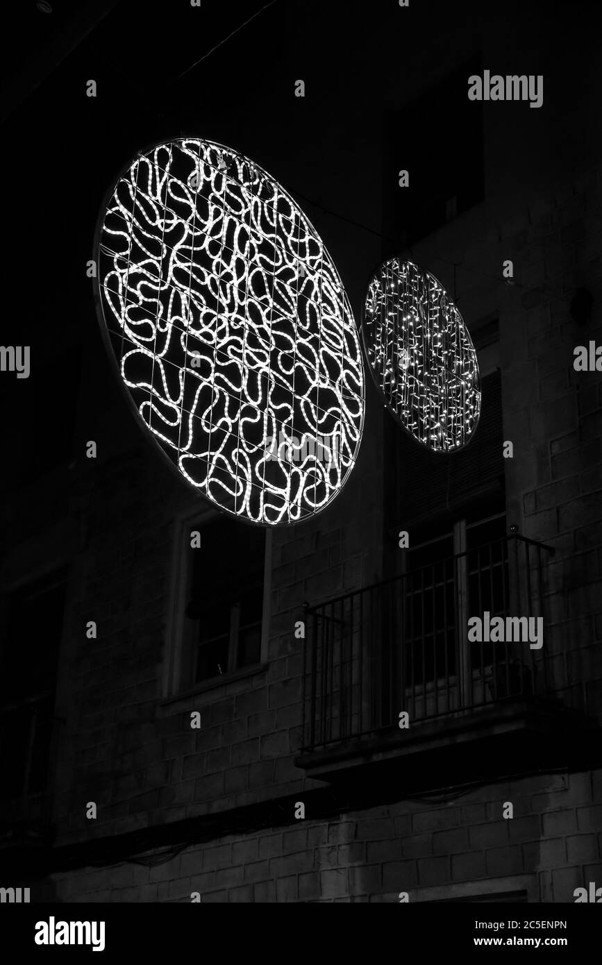Große Metallscheibe, mit einem großen LED-Licht-Schlauch innen, mehrmals drehbar, hängt von der Spitze einer Straße in Barcelona, Spanien Stockfoto