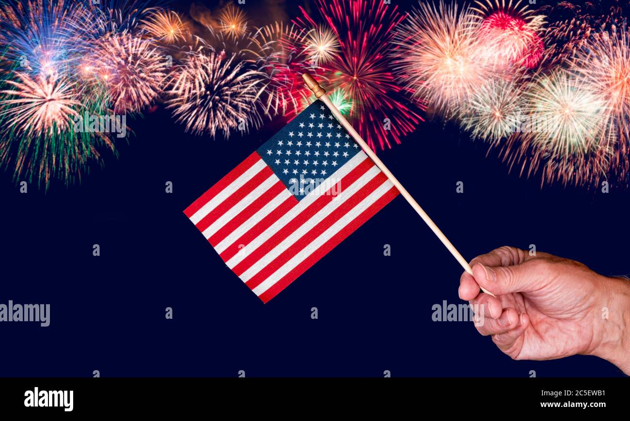 Senior mans Hand hält ein kleines Spielzeug USA Flagge und Ausschnitt vor Feuerwerk Hintergrund Stockfoto
