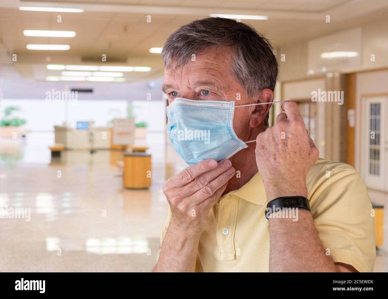 Leitender Kaukasusmann, der seine Gesichtsmaske anpasst und besorgt über die Coronavirus-Epidemie schaut. Composite innerhalb eines Einkaufszentrums Stockfoto