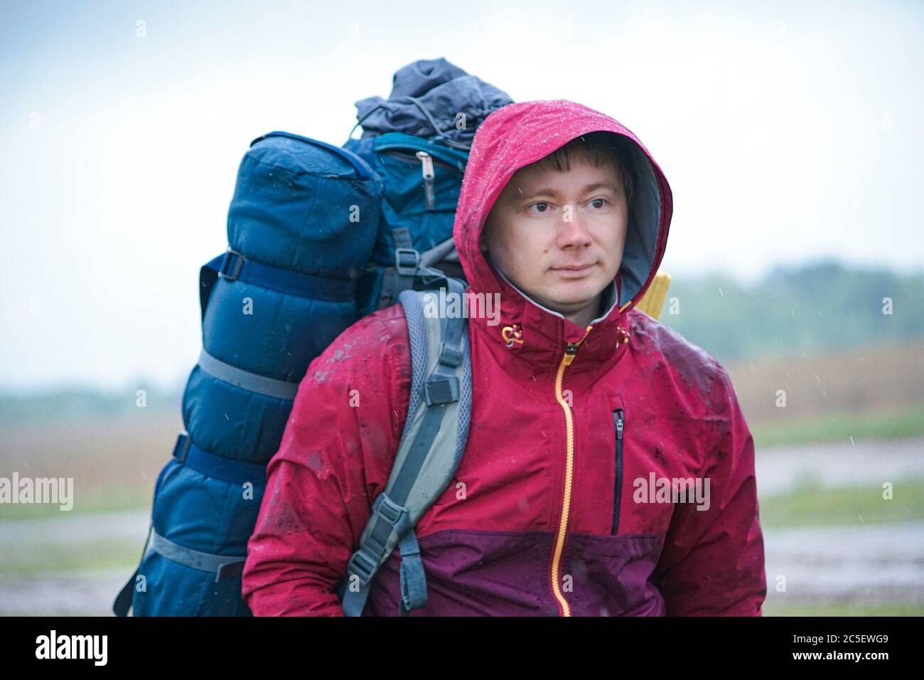 Ein Kerl mit Rucksack steht in der Nähe der Straße, eine Fahrt zu fangen. Touristen stimmen bei der Straße im Regen Stockfoto