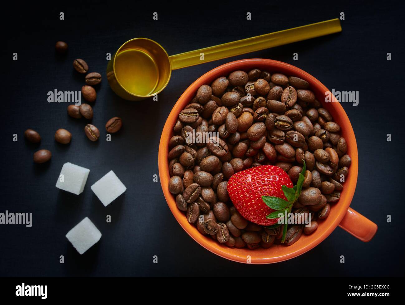 Tasse mit Kaffeebohnen und Erdbeeren, Messlöffel, dunkler Hintergrund Stockfoto