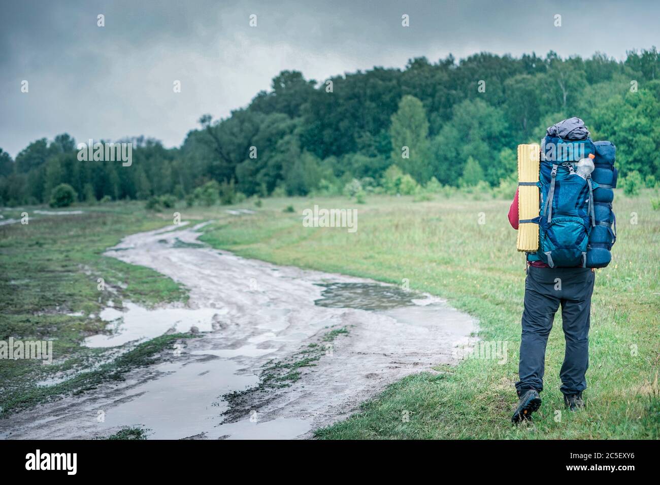 Guy Tourist Wanderer läuft entlang der Schotterstraße mit einem Rucksack in einer roten Jacke im Regen Stockfoto