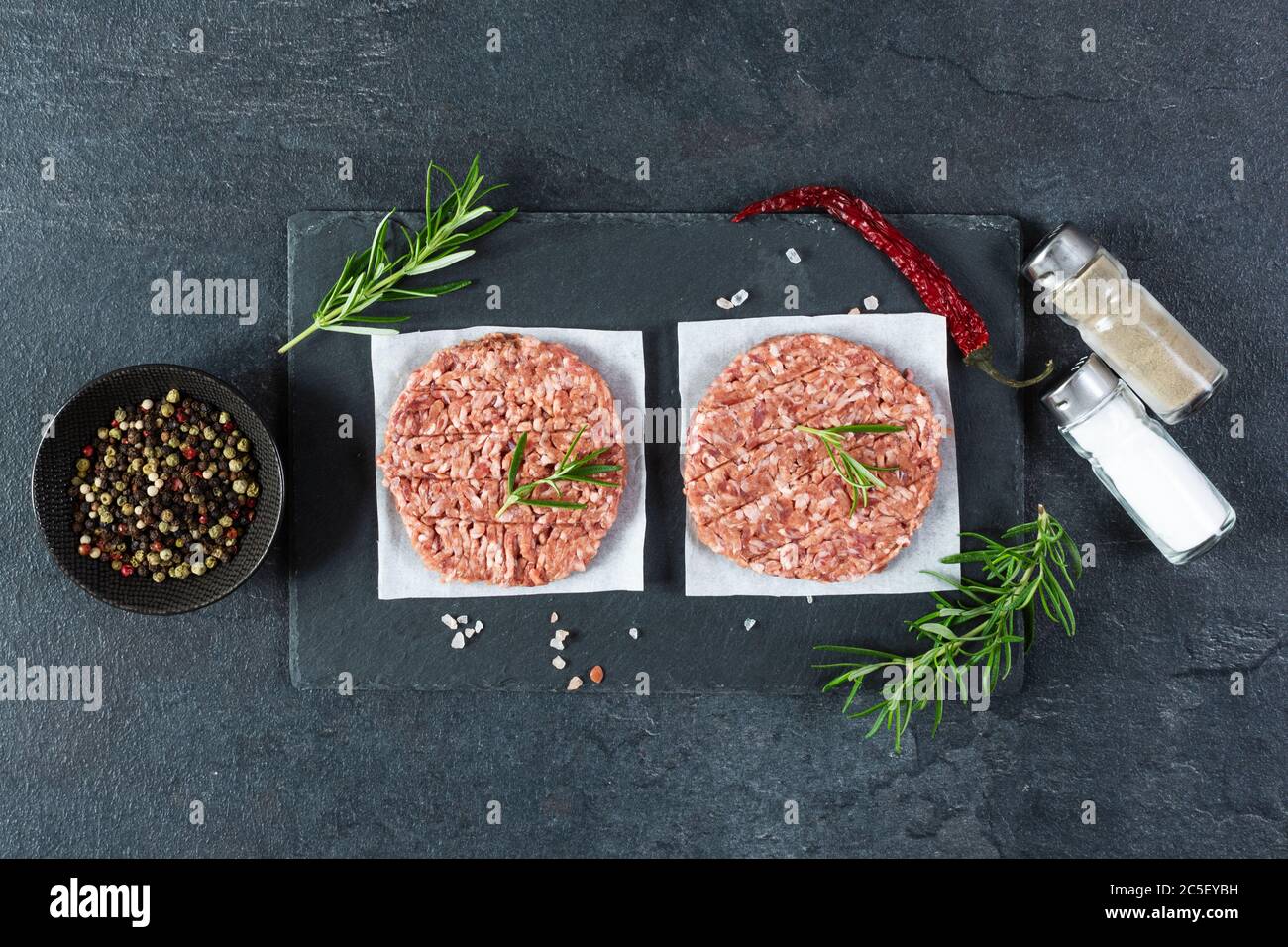 Rohe Burger-Cutlets aus Hackfleisch frisch treffen mit Rosmarin und Chili auf einem Schieferbrett Draufsicht. Zutaten für die Herstellung von Burgern. Stockfoto