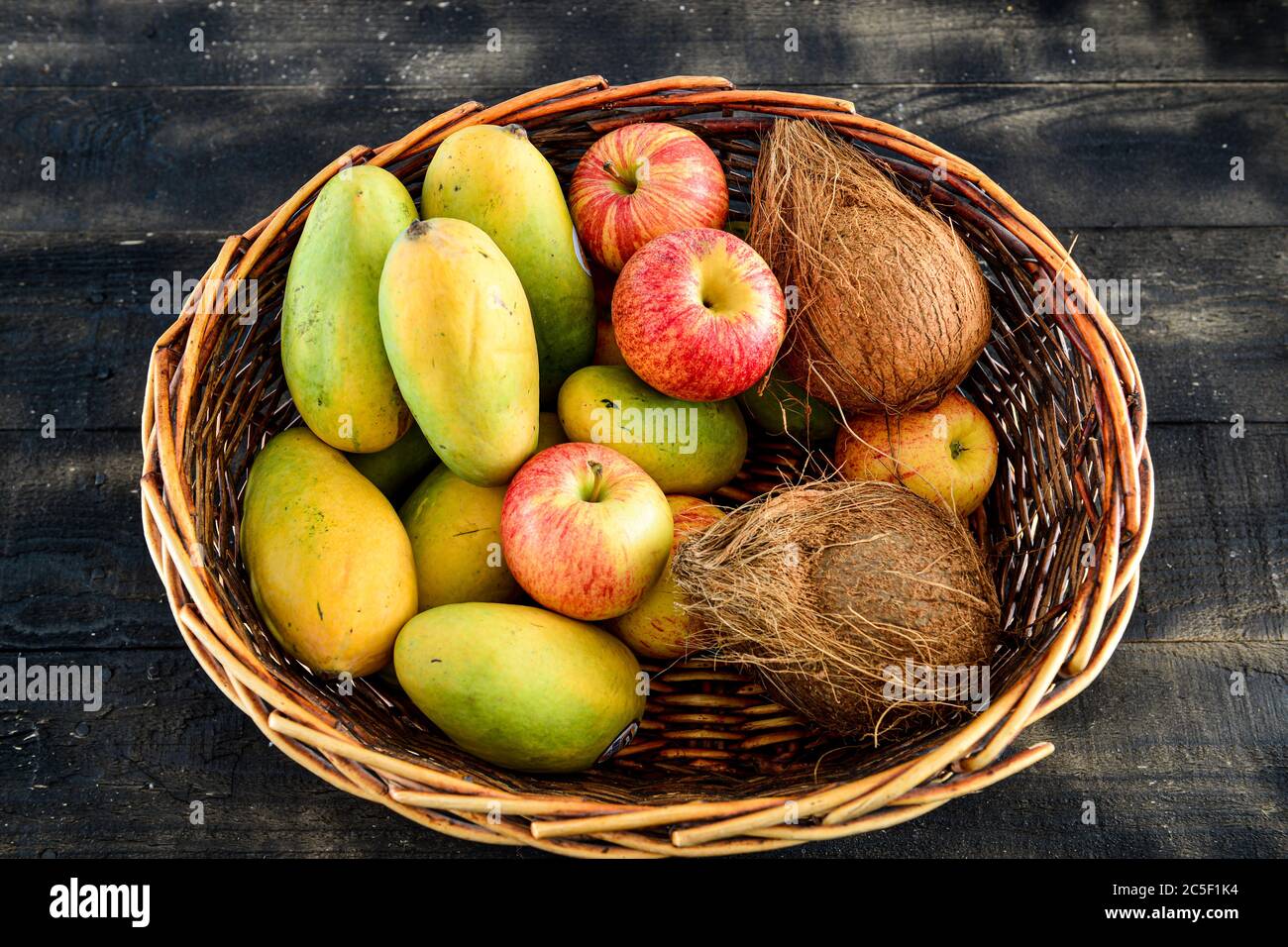 Früchte, Mango, Kokosnuss, Apfel in einem Korb auf schwarzem Holzgrund mischen Stockfoto