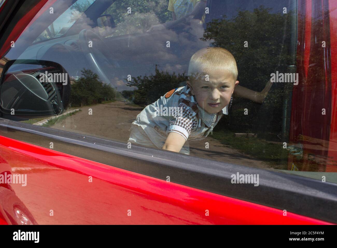 Ein Junge in einem roten Auto geschlossen und versucht, durch die Türen Auto zu bekommen Stockfoto