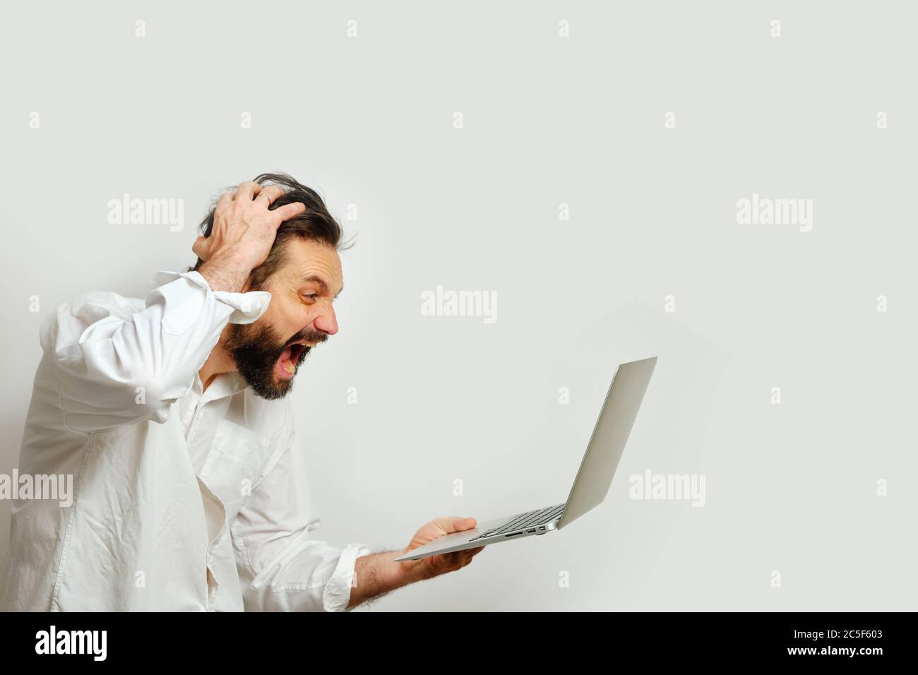 Mann hält sich den Kopf fest und blickt verzweifelt auf einen Laptop-Monitor, der auf weißem Hintergrund isoliert ist. Das Konzept der Emotionen und Finanzkrise. Stockfoto