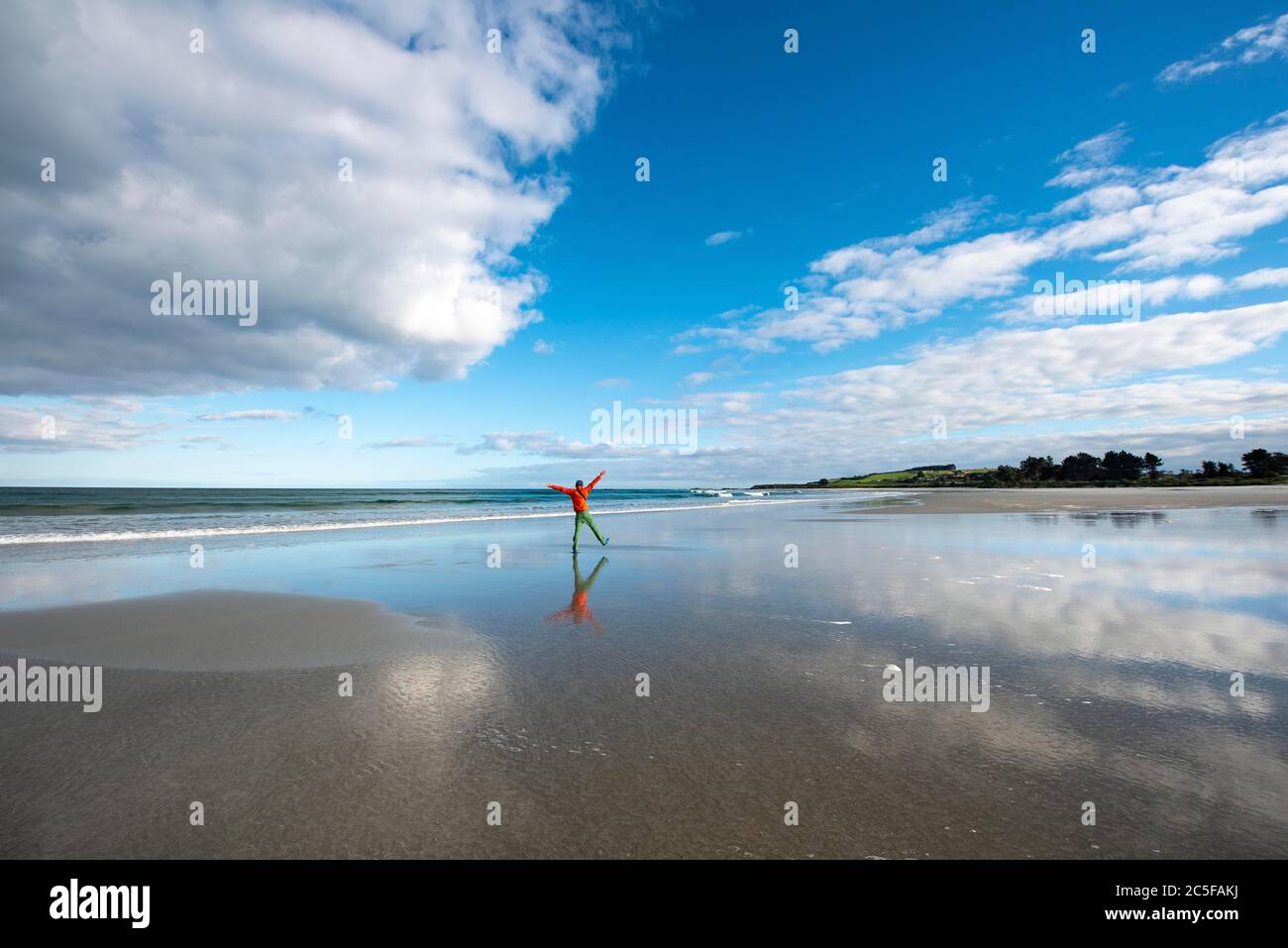 Reflexion, junger Mann, der bei Ebbe am breiten Sandstrand, Taieri Beach, Südinsel, Neuseeland, spazierengeht Stockfoto