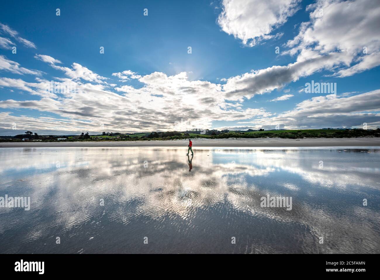 Reflexion, junger Mann, der bei Ebbe am breiten Sandstrand, Taieri Beach, Südinsel, Neuseeland, spazierengeht Stockfoto