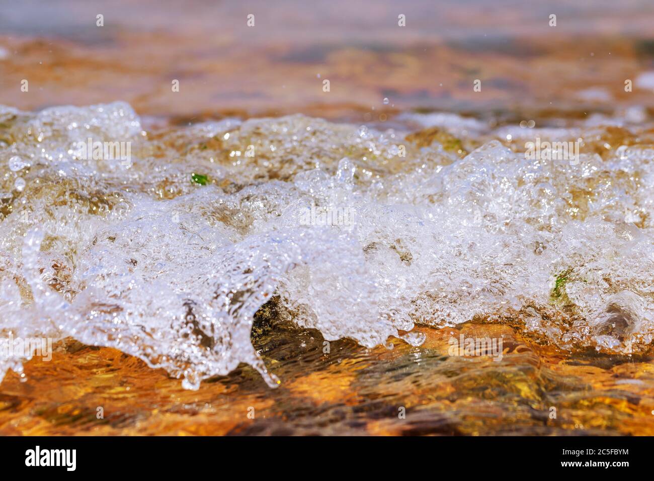 Hintergrund mit Meereswellen über bunten Felsen und Steinen. Selektiver Fokus. Stockfoto