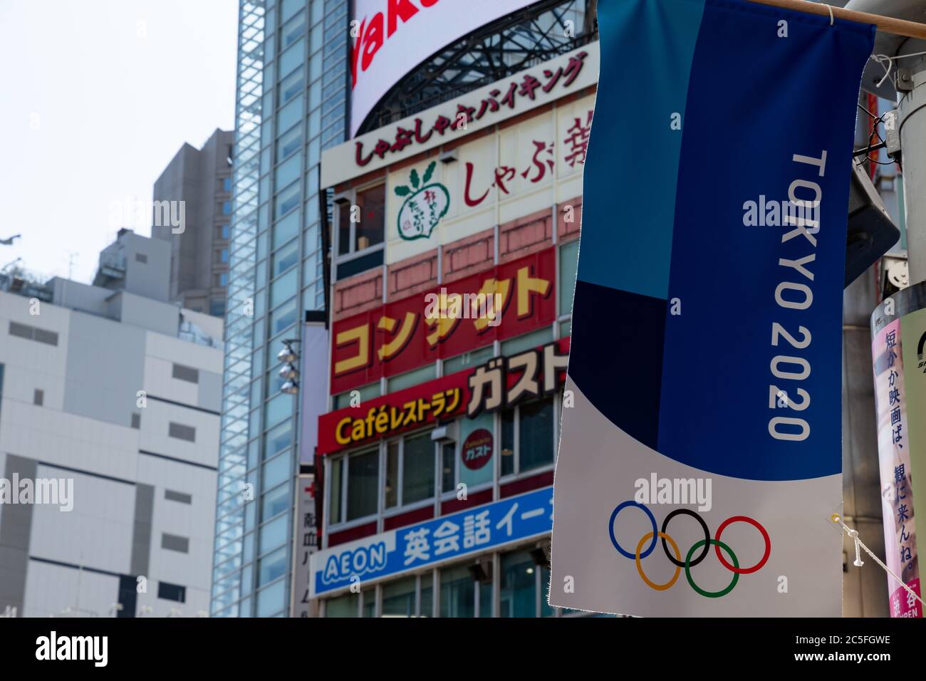 Tokyo 2020 Banner flattert im Wind. Shibuya Gebäude mit Werbung im Hintergrund. Stockfoto