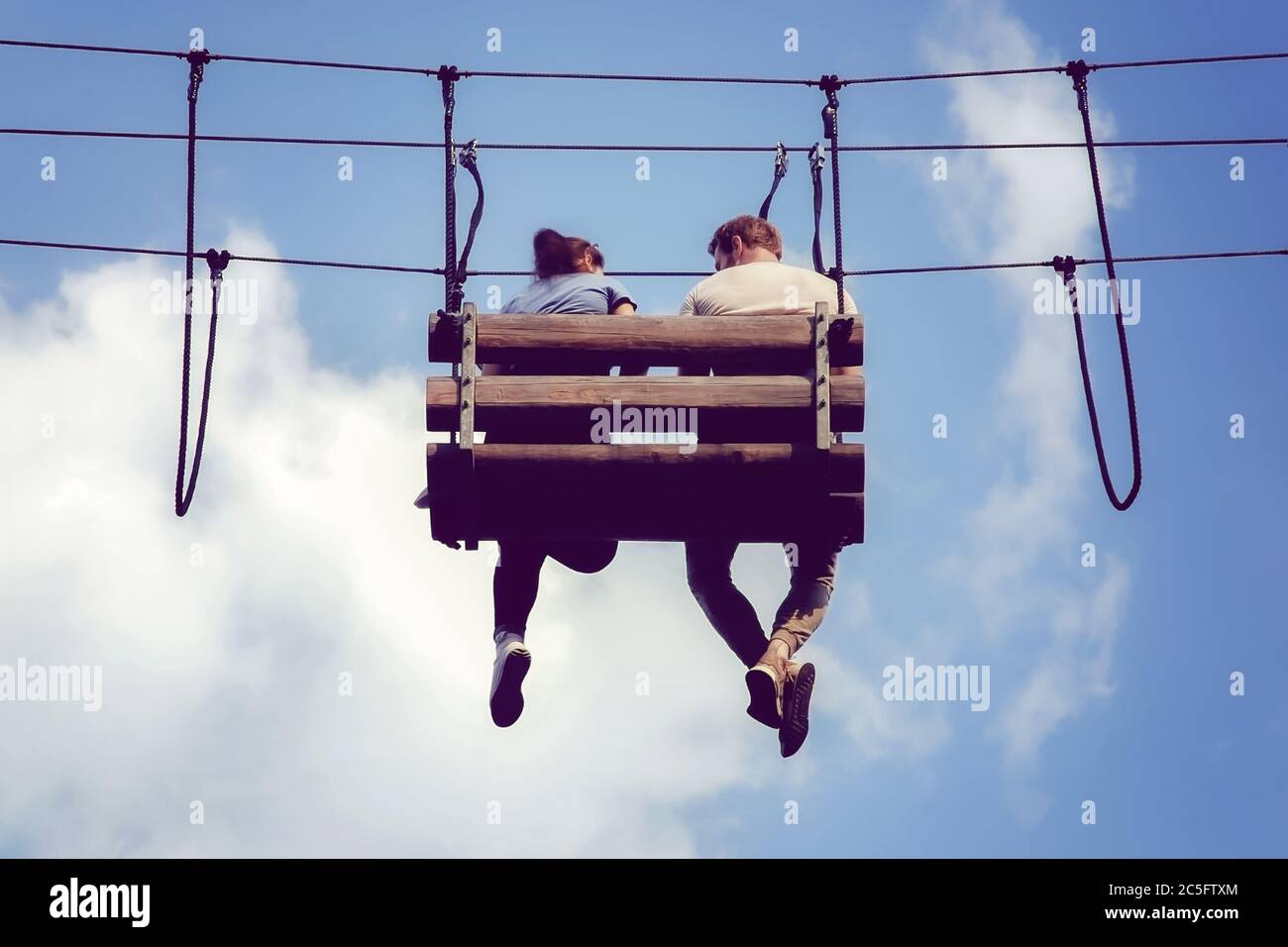 Moskau 10/07/2019 Junges Paar sitzen baumelnden Beinen auf einer hängenden Bank im Abenteuer Seilpark. Romantische Treffen am Himmel. Stockfoto