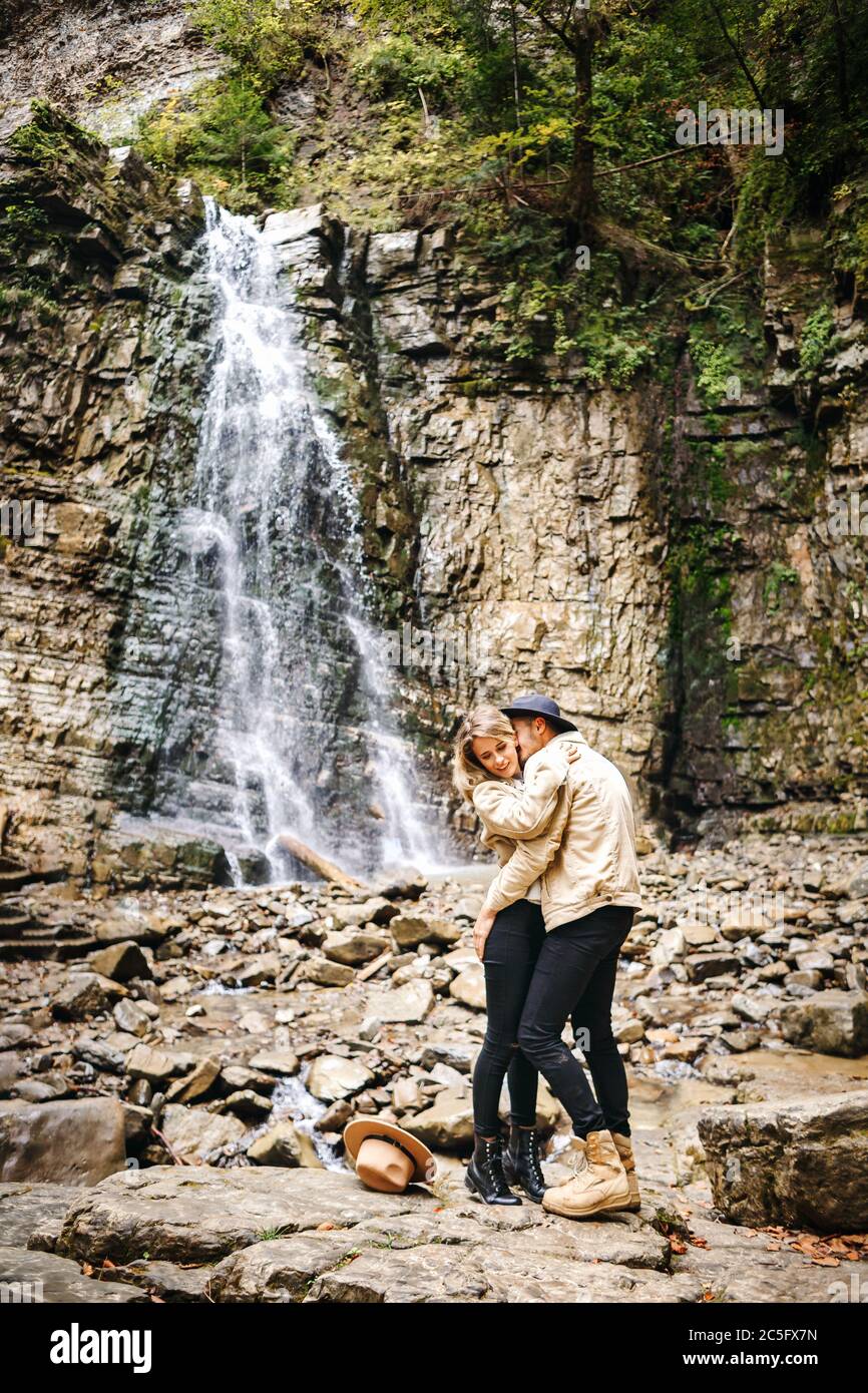 Junges und schönes Paar am Bergwasserfall - Glückliche Touristen, die Berge besuchen. Liebe. Touristen in Hüten. Militärische Mode Stockfoto