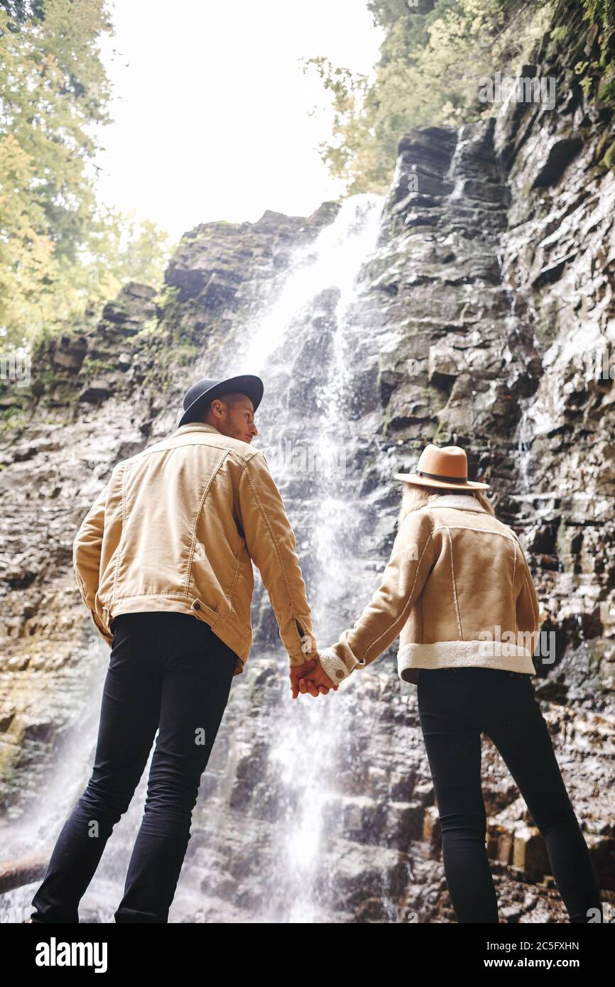 Junges und schönes Paar am Bergwasserfall - Glückliche Touristen, die Berge besuchen. Liebe. Touristen in Hüten. Militärische Mode Stockfoto