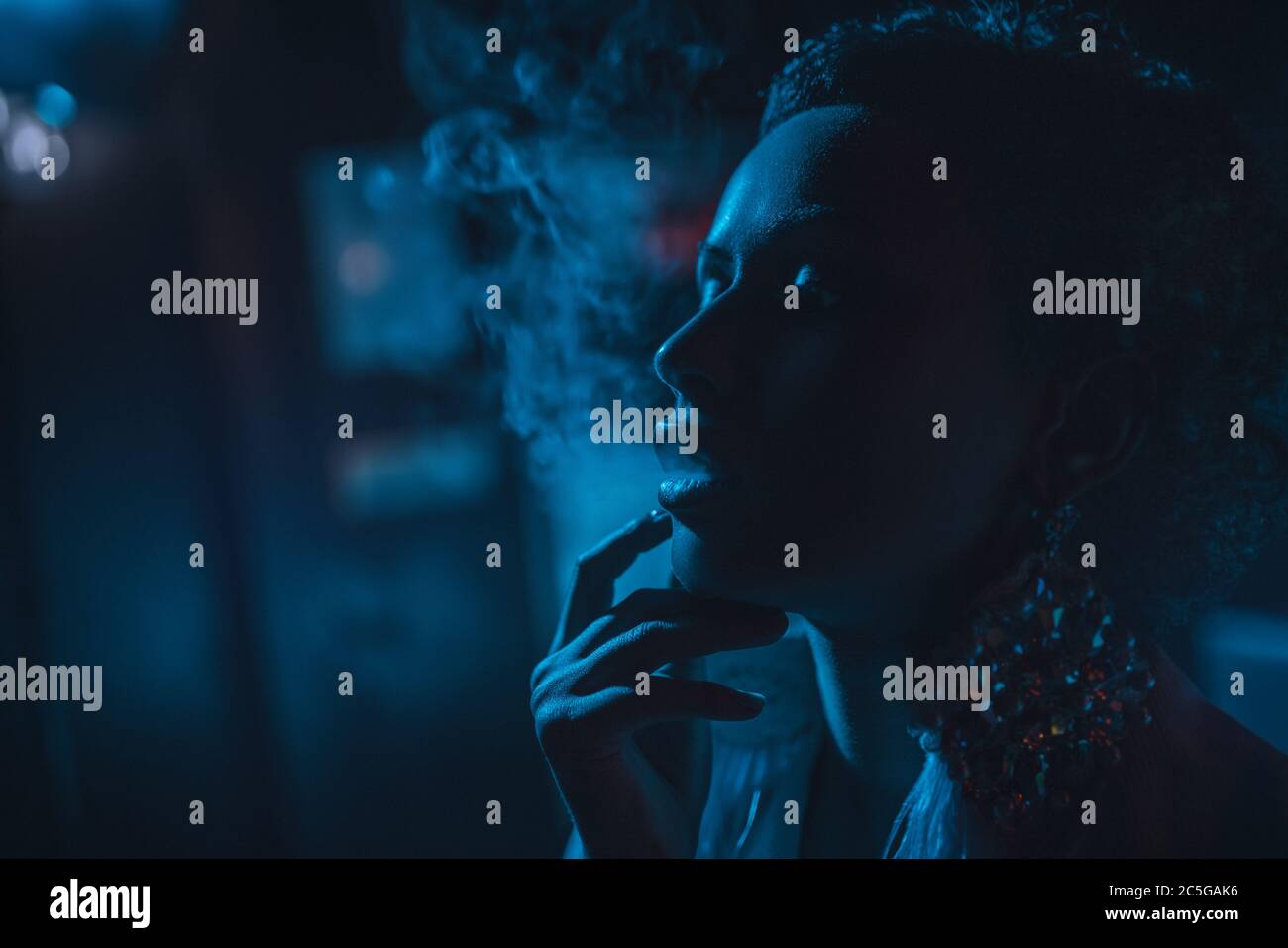 Junge rauchende Frau dunkel Nacht Porträt. Blauton. Stockfoto