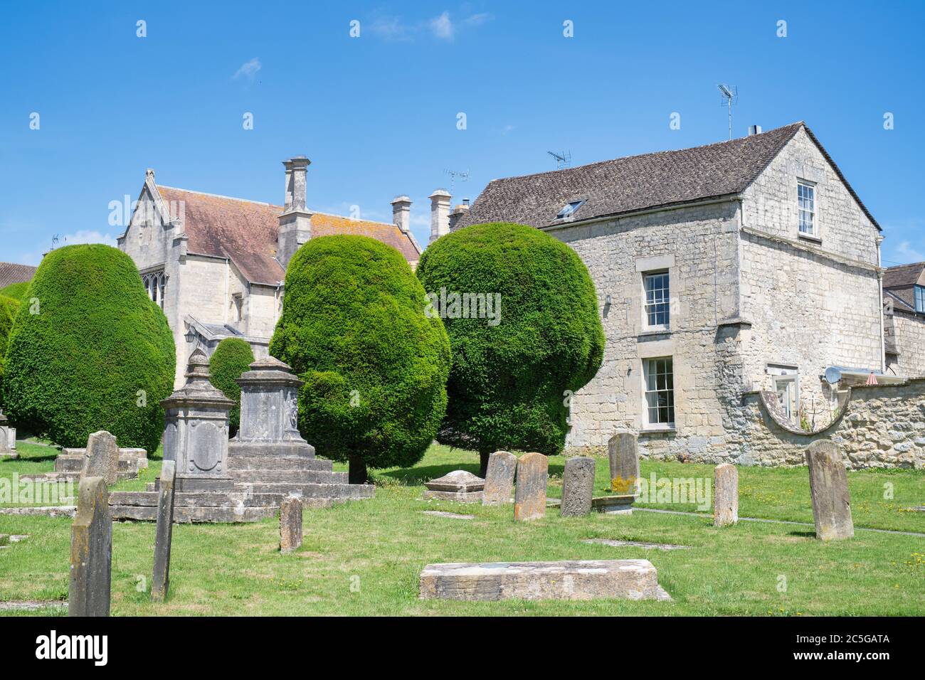 Eibe Bäume und Grabsteine in St. Marys Kirchhof in der Sonne. Painswick, Cotswolds, Gloucestershire, England Stockfoto