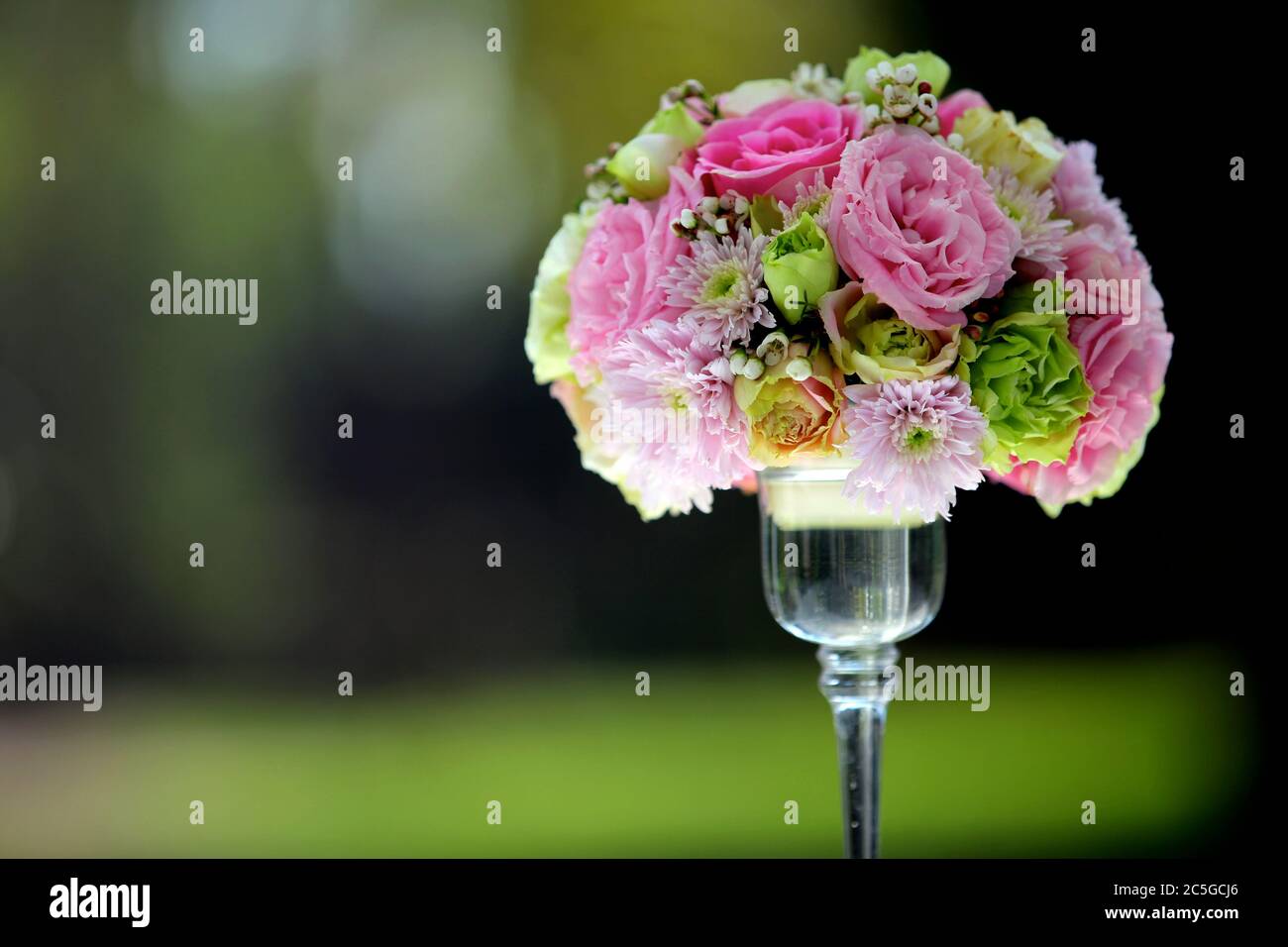 Ein großer Blumenstrauß und bunt in einer klaren Glasvase auf einem verschwommenen grünen Hintergrund, in Hochzeitszeremonien verwendet. Stockfoto