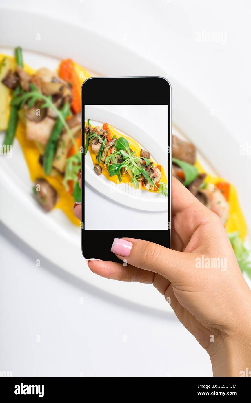 Fotografieren von Essen Konzept - Frau macht Bild von gebackenen Fisch King Clip mit Gemüse und Sauce, von einem grünen Salat in weißem Teller dekoriert. Stockfoto