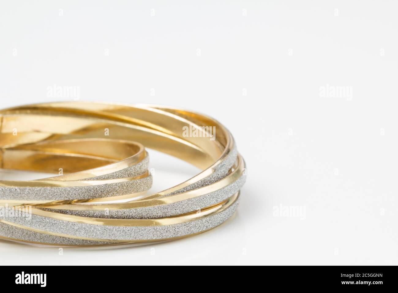 Nahaufnahme von goldenen Armreifen mit silbernem Glitter-Streifen auf weißem Hintergrund mit Kopierfläche. Stockfoto