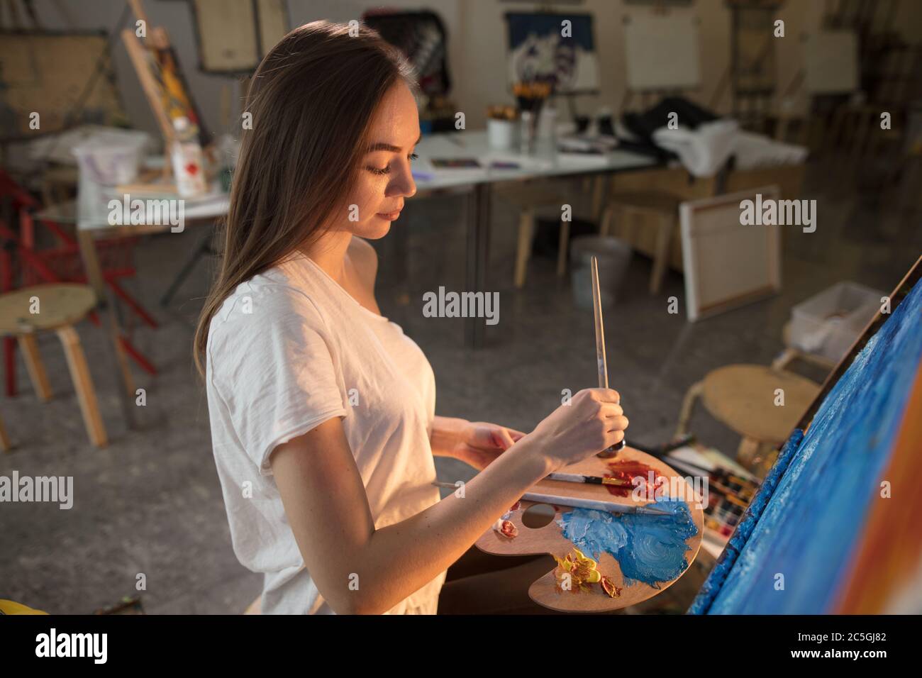 Langhaarige Künstlerin Frau mit einer Palette in den Händen bleiben bis in die Nacht in der Werkstatt wollen Bild zu beenden Stockfoto