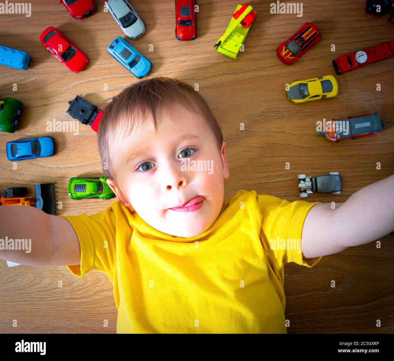 Niedlichen kleinen Jungen spielen mit vielen Spielzeug Autos drinnen. Kind trägt gelbes Hemd. Glücklich Vorschulkinder Spaß zu Hause oder im Kindergarten. Große Kollektion Stockfoto