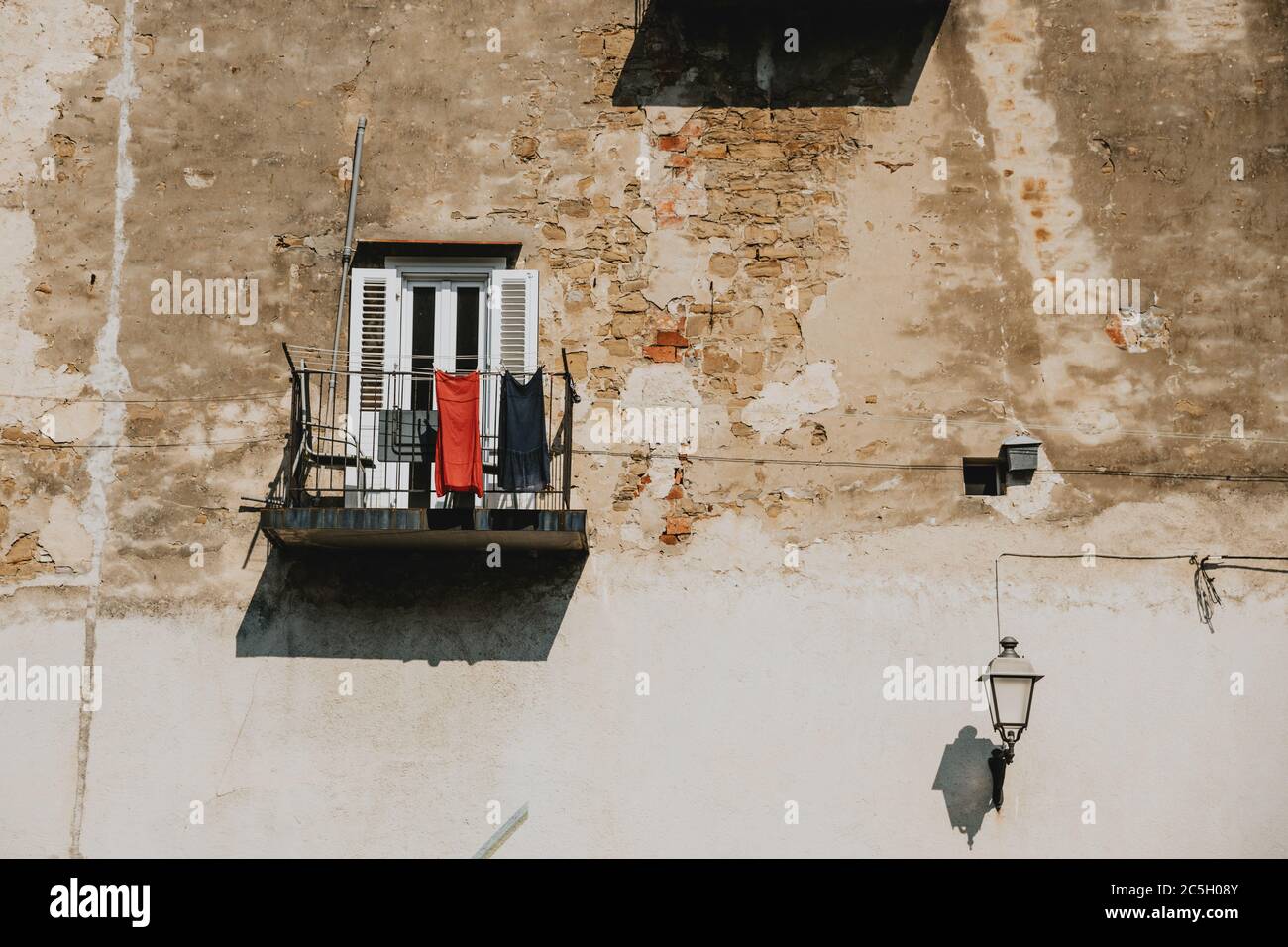 Rote und blaue Kleider hängen auf dem Metallgeländer des kleinen Balkons des alten Hauses mit der Wand mit rissiger Fassade in Slowenien Küstenstadt Piran Stockfoto