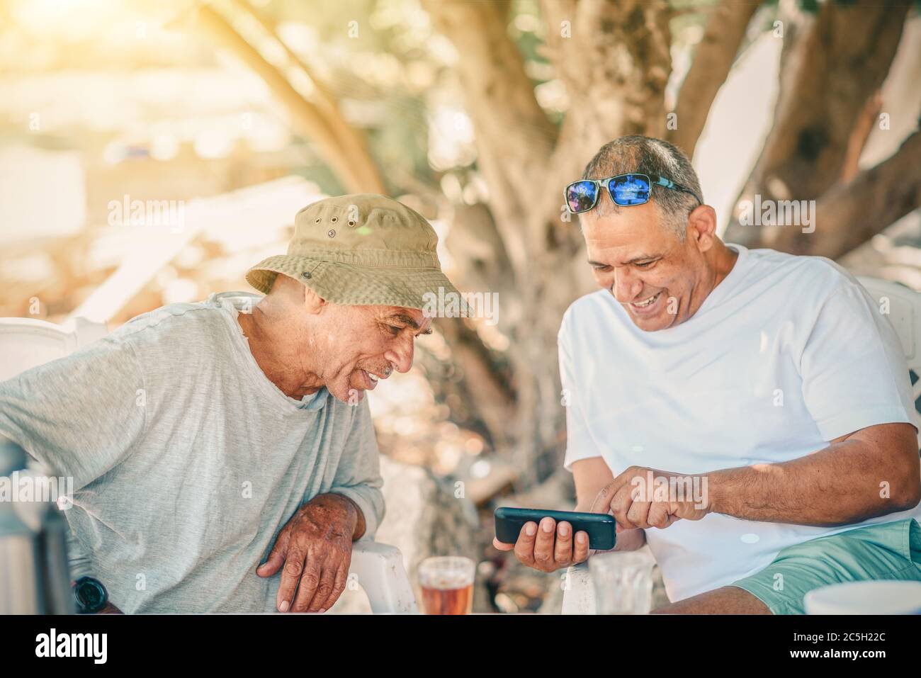 Zwei positive lächelnde Silber Surfer Senior Mann verwenden Smartphone und Tee trinken. Aktive gesunde Senioren Spaß im Garten. Stockfoto