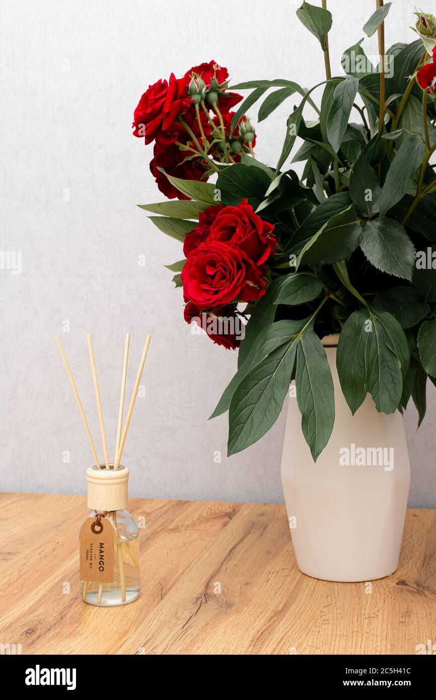 Aroma-Schilfdiffusor im Innenraum. Rote Rosenblumen in Vase auf Holztisch mit Kopierraum Stockfoto